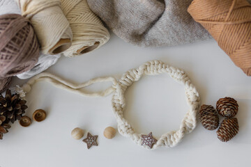 Winter table decor. White macrame wreath, cones, balls of thread and gray knitted sweater on white table.