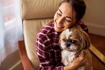 Happy woman enjoying with her dog in armchair at home.