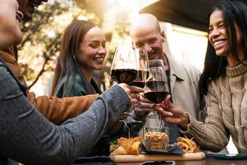 Young smiling friends toasting red wine at restaurant pub at happy hour with appetizers  - Happy people having fun together at winery bar and eating food  - Dinning life style concept. focus on glass 