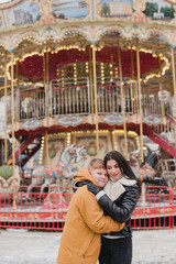Obraz premium Caucasian mother and son in warm cozy clothes walk outdoors on festive city streets. Family walks at the fair as snow falls. Cold happy winter day. Holidays, Christmas, New Year, love concept.