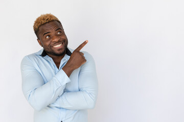 Portrait of excited young man pointing at ad. Happy young male model with blond hair in light blue shirt looking away, smiling and showing ads with finger. Advertisement concept