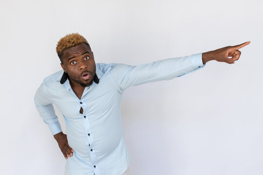 Portrait of displeased African American man pointing away. Angry young male model with blond curly hair in light blue shirt looking at camera, chasing someone away. Conflict, argument concept