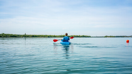 A man in a blue boat kayaking on a lake in summer