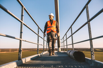 A metal construction worker is walking on the height and smiling while looking at horizon.
