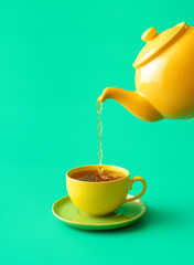 Pouring tea in a cup minimalist on a green background.