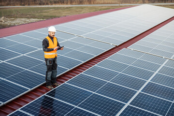 A supervisor is standing on the roof and checking on solar panels over tablet.