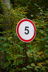 A sign indicating a speed limit of five miles per hour is in the park, in the forest.