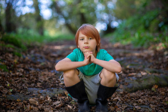 a boy of nine sits on a path in the woods alone