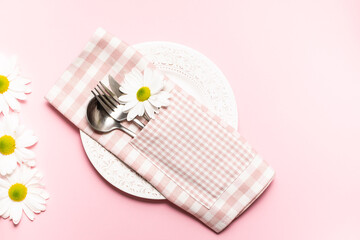 Country style tabble setting with plate, checkered napking, cutlery set and fresh chamomile flowers on light rose background with copy space for your design.