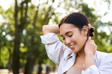 Beautiful young woman tying her hair while walking in park, smiling romantic, enjoying warm day