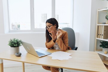 Business woman working in the office at her desk with a laptop in a beige suit and white shirt with glasses online video chat, teacher teacher engaging with college students