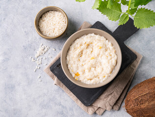 Rice porridge with fruit and coconut milk in bowl on a blue background. The concept of a vegan delicious, nutritious and healthy breakfast.