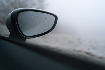 Close-up with the frozen side mirror of a car during winter season, lack of visibility and high risk of accident caused by ice.