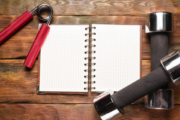 Blank page notepad and dumbbells on the wooden background. Exercise list mockup.