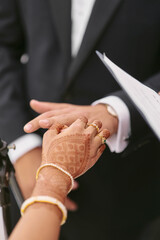 Faceless bride with Hindu drawings of henna on her hands put a wedding ring on groom`s finger during a wedding ceremony
