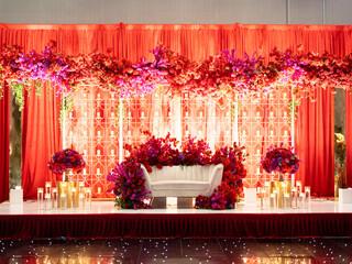 Front view of amazing Hindu wedding arch decorated by red flowers with white sofa for groom and...