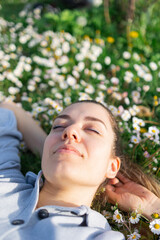 Beautiful young woman lying down in daisy field. Resting, relaxing. She is so happy. 