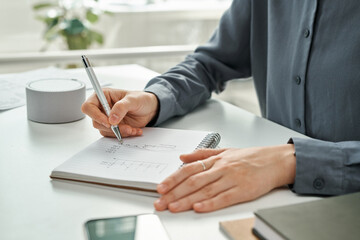 Close-up of manager writing financial strategy in notepad while working at office