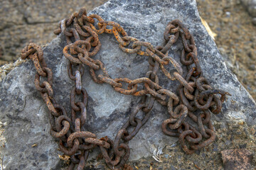 A length of heavy rusty chain tangled up on a boulder, daytime, sunny, nobody