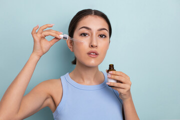 portrait beautiful young woman in blue undershirt does drips anti wrinkle oil from a pipette and holding a bottle in his hand, moisturizes the skin. skin rejuvenation procedure at home.