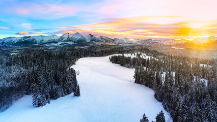 Fototapeta premium Snow capped mountains in the winter, aerial view. Aerial panorama of winter mountain landscape and colorful sunset sky. Tatra high mountains and magical unspoiled scenery.