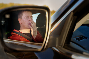 A tired driver yawns while covering his mouth with his hand while sitting at the wheel.