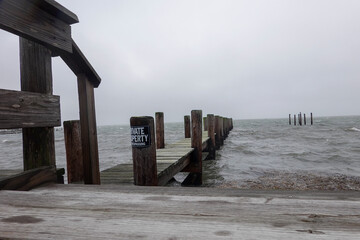 Rough ocean surf pounds the wooden dock with a no trespassing sign at a deserted marina during a storm