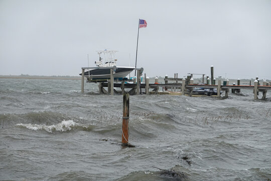 Rough ocean surf pounds the wooden dock at a deserted marina during a storm with a boat up out of the water - Powered by Adobe