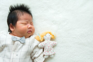 寝ている産後1か月0歳の新生児と右隣に置いた女の子のぬいぐるみと白背景の左寄りの写真