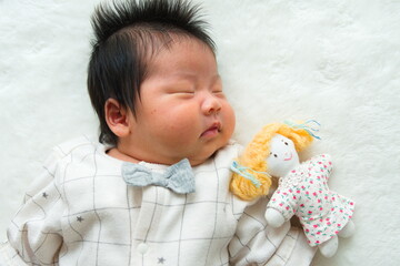 寝ている産後1か月0歳の新生児と左隣に置いた女の子のぬいぐるみと白背景で撮影した写真