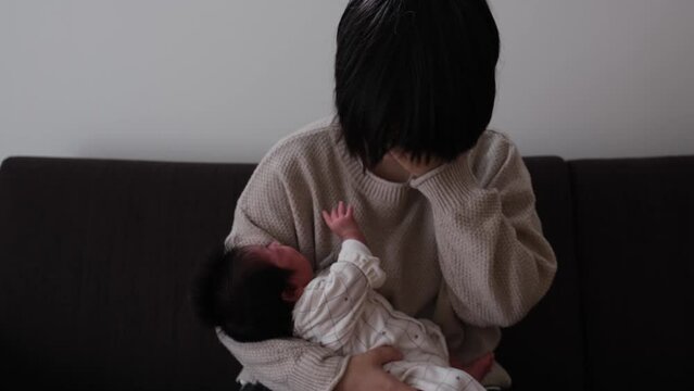 大泣きしている産後1か月0歳の新生児を母親が抱っこしながら顔に手を当てている様子の動画