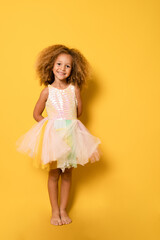 Happy child girl wearing a festive dress standing isolated over yellow background.