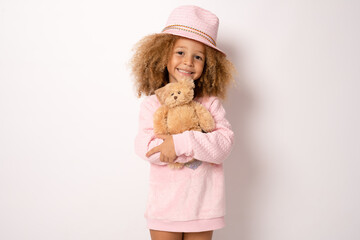 Little child girl wearing straw hat is hugging teddy bear isolated over white background.