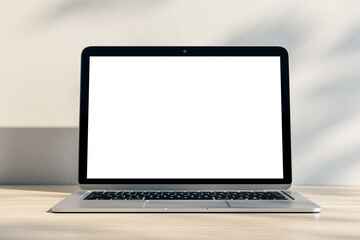 Fototapeta premium Closeup of modern laptop with blank white screen and place for your logo or text on light wooden table and sunlit wall background. 3D rendering, mock up