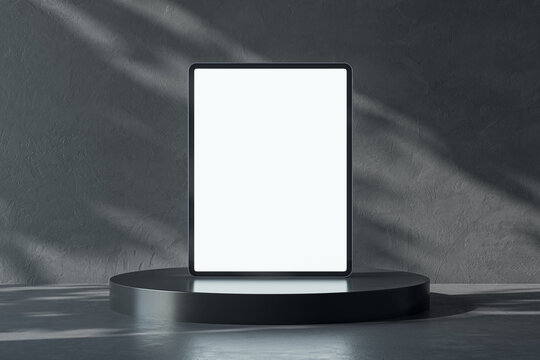 Front view on blank white digital tablet screen with place for your logo or text on dark glossy stand on abstract sunlit concrete background. 3D rendering, mock up