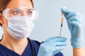 Doctor in surgical mask and gloves preparing syringe for injection