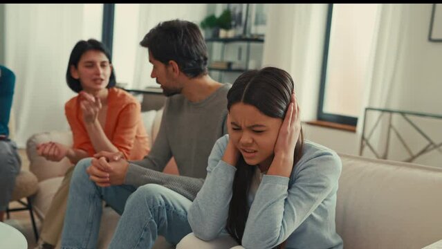 Psychological problem of parents. Parents swearing at a psychologist's appointment while the teenage daughter covers her ears with her hands. Family therapy.