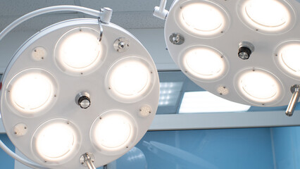 In the hospital, a surgical lamp shines under the ceiling above the surgical table. Two large round...