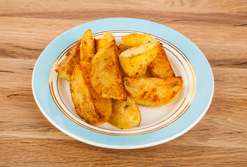 Fried potatoes in a plate on a wooden background.