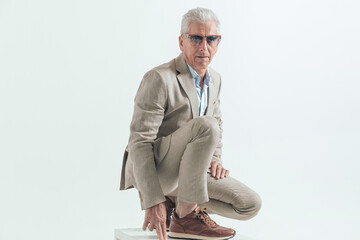 good looking man in his 60s crouching and posing with hands in fashion pose