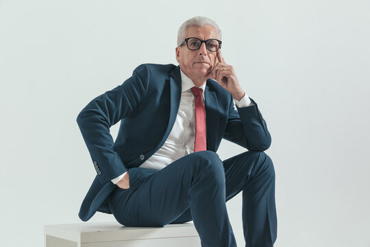 seated elegant man with grey hair touching face and thinking