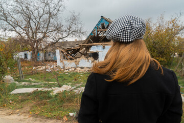 Countryside. The girl looks at the house destroyed by shelling. War in Ukraine. Russian invasion of Ukraine. Terror of the civilian population. War crimes