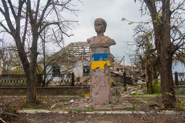 Monument damaged by shelling against the background of a destroyed house. War in Ukraine. Russian...