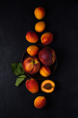 ripe fresh bright apricots and peaches lie in scattering on a clay plate and on a dark surface. view from above. artistic moody still life