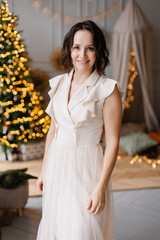 beautiful festive portrait of a woman. Christmas bokeh home background. Waiting for a miracle make a wish under the Christmas tree. Charming smile. Restrained colors. New Year's holiday atmosphere