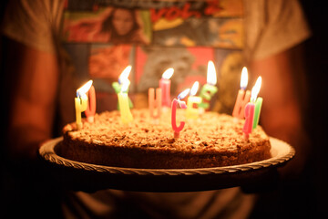 Festive cake with burning candles on the hands of a person close-up, holiday, birthday.