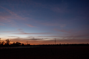 Beautiful dramatic orange and blue cloud and sky after storm and raining over agricultural field and high voltage tower on countryside in Germany. Nimbostratus cloud during sunset. 