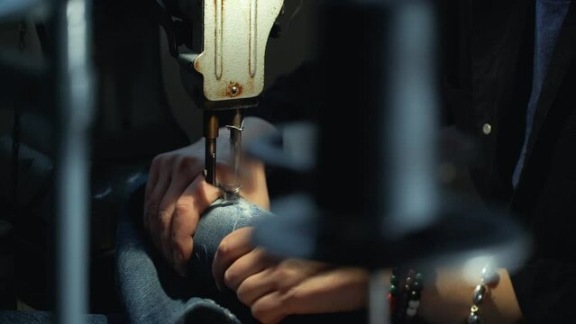A female tailor seamstress repair old jeans with vintage darning machine in a workshop repairing denim clothes. Small family business, tailoring and repair of clothes, handmade, startup. Close-up