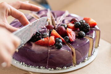 The girl cuts a cheesecake with fruits, strawberries, blackberries, blueberries, cake, holiday.