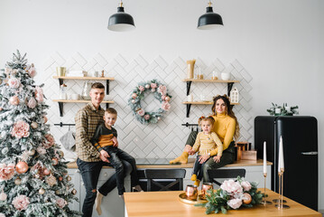 Happy family couple with two children relaxing together in kitchen. Christmas tree and home decorated interior. Celebration New Year and Christmas. Mother, father, daughter and son having breakfast.